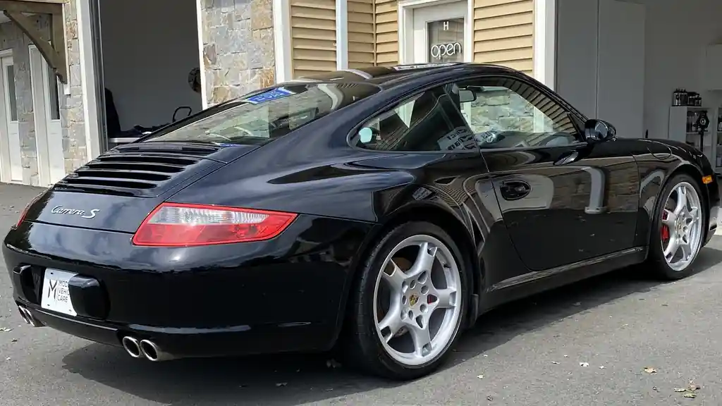 Black Porsche 911 Carrera S, rear three-quarter, outside the shop