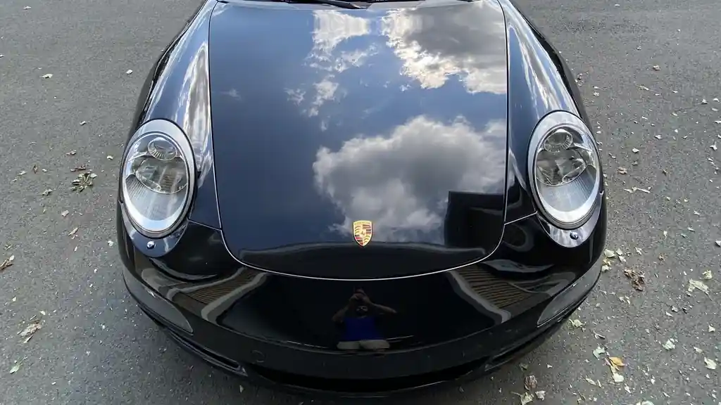 Black Porsche 911 hood reflecting clouds after correction