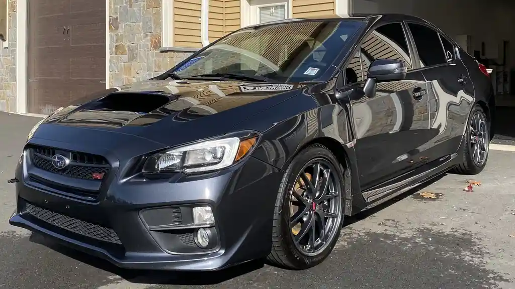 Charcoal Subaru WRX STI with a black hood, street reflected in the paint